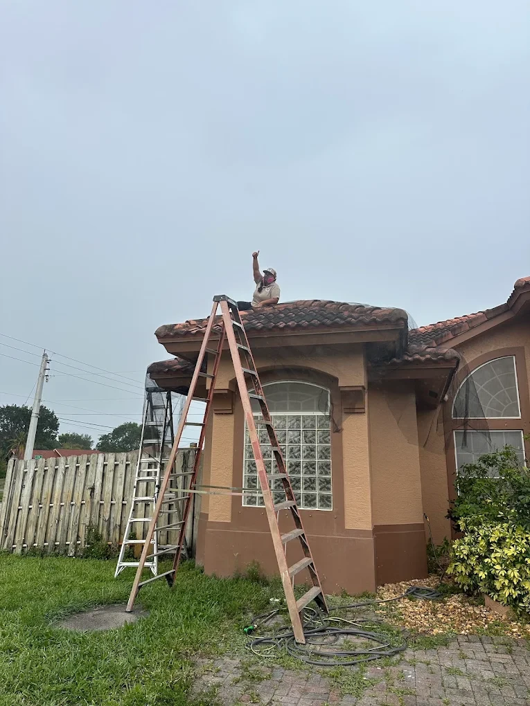 A Swift Wildlife technician working a tile roofline with ladders at a Treasure Coast waterfront home — iguana removal and exclusion